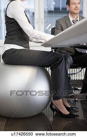 Stock Image - Businesswoman sitting on gym ball. Fotosearch