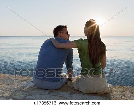 Stock Image - Couple by sea watching sun set. Fotosearch