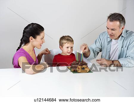 Picture - Couple lighting candles on cake for son. Fotosearch