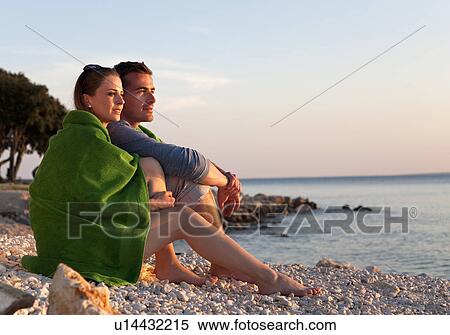 Stock Photography - Couple sitting at beach. Fotosearch