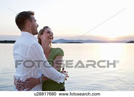 Stock Image - Couple watching sun set at beach. Fotosearch