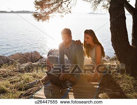Couple with wireless laptop by sea View Large Photo Image Stock Photography - Couple with wireless laptop by sea. Fotosearch