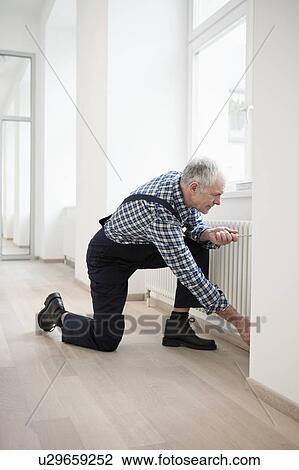 Stock Image - Craftsman fixing heater. Fotosearch