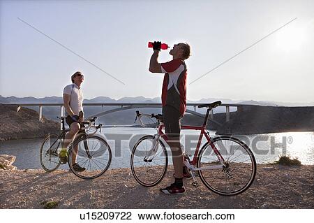 Stock Image - Cyclists drinking water by sea. Fotosearch