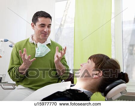 Stock Image - Dentist explaining to patient in surgery. Fotosearch