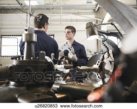 Stock Image - Engineer Teaching Apprentice In Workshop. Fotosearch