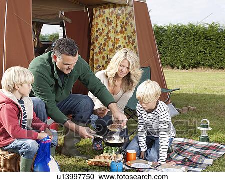Stock Image - Family cooking meal outdoors. Fotosearch