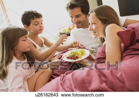 Stock Image - Family having breakfast in bed. Fotosearch
