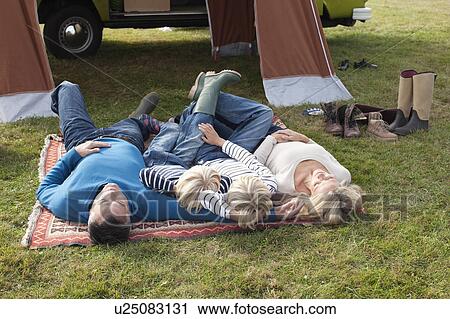 Stock Image - Family lying down in front of tent. Fotosearch