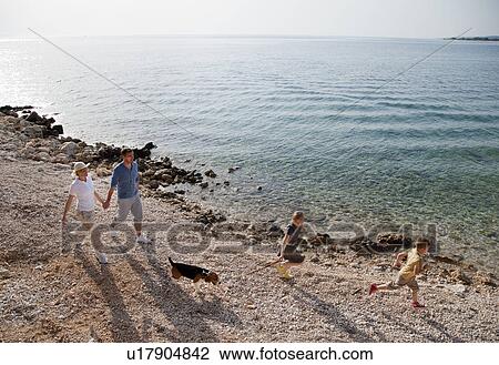 Stock Image - Family with dog running at the beach. Fotosearch