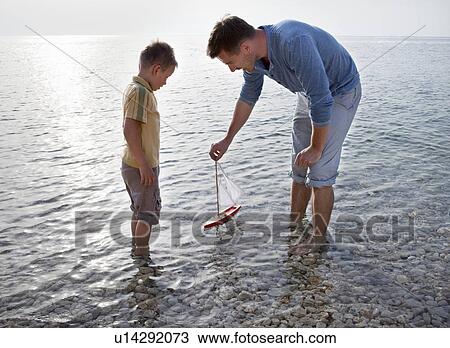Stock Image - Father and son with toy boat at beach. Fotosearch