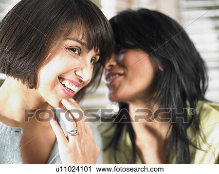 Stock Image - Girlfriends sharing a secret. Fotosearch