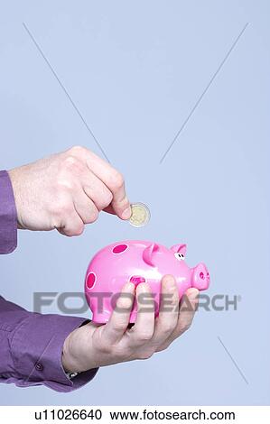 Stock Image - hand dropping a coin in a piggy box. Fotosearch