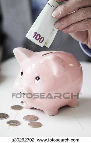 Stock Image - Hand putting banknote into piggy bank. Fotosearch