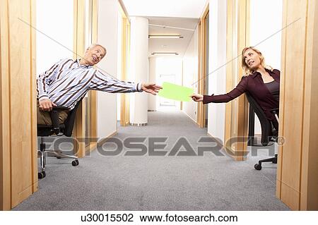 Stock Image - Handing a green paper to the colleague. Fotosearch