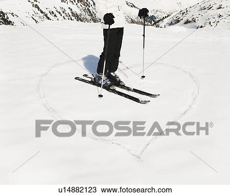 Stock Image - Heart shape in snow with woman skier. Fotosearch