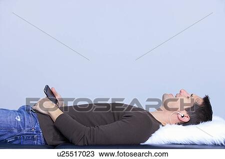 Stock Image - lying man listing to music, and singing. Fotosearch