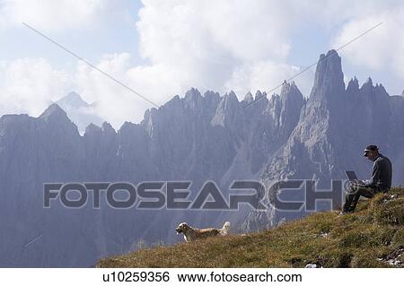 Stock Photograph - Man and dog in mountains with laptop. Fotosearch