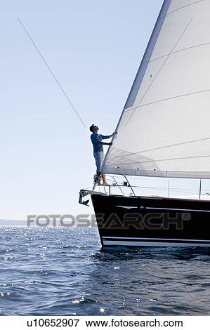 Stock Photo - Man checking sail on yacht. Fotosearch