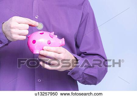 Stock Image - man dropping a coin in a piggy box . Fotosearch