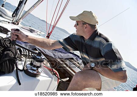 Stock Photography - Man hoisting sail on yacht. Fotosearch