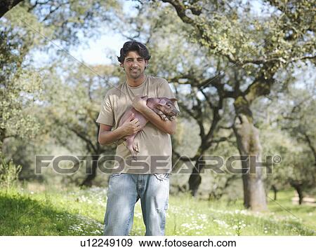 Stock Photo - Man holding a piglet in field on farm. Fotosearch