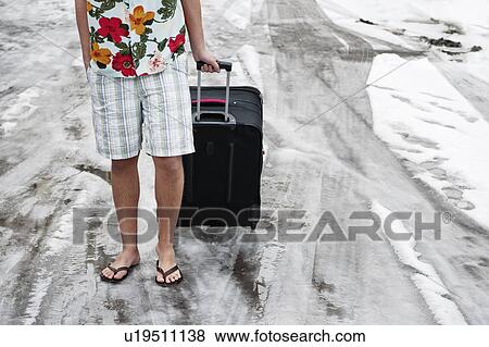 Stock Photo - Man in summerwear with suitcase in snow. Fotosearch