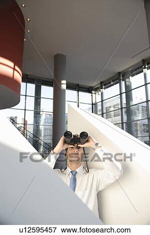 Man looking through binoculars in office View Large Photo Image Stock Photo - Man looking through binoculars in office. Fotosearch