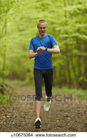 Picture - Man running, looking at sports watch. Fotosearch
