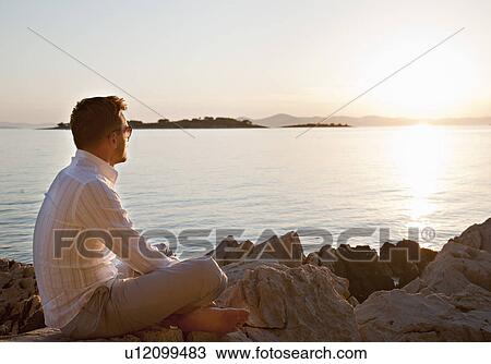 Man watching sun set at rocky beach View Large Photo Image Stock Image - Man watching sun set at rocky beach. Fotosearch