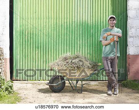 Stock Image - Man with wheelbarrow full of hay. Fotosearch