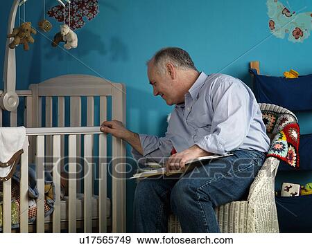 Stock Photo - Mature male sitting with baby in cot. Fotosearch