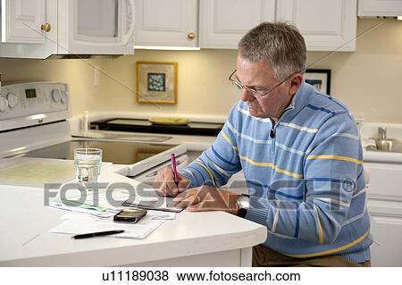 Stock Photo - Mature man paying bills in kitchen. Fotosearch