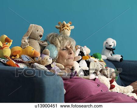 Stock Image - Mature woman asleep surrounded by toys. Fotosearch