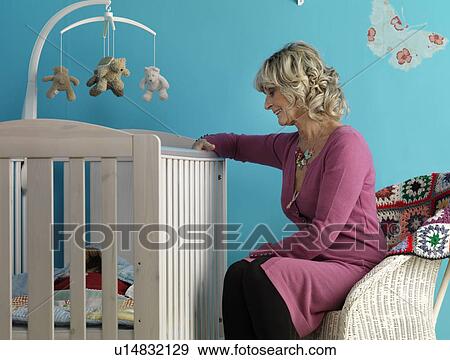 Stock Photo - Mature woman sitting next to cot. Fotosearch