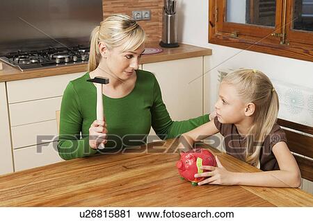 Stock Image - Mother and daughter crack a piggy bank. Fotosearch