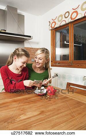 Stock Image - Mother and daughter crack a piggy bank. Fotosearch