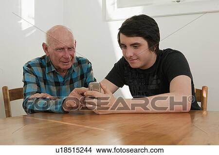 Picture - Old man looking at phone with grandson. Fotosearch