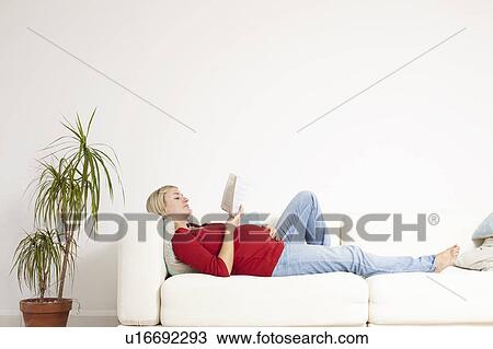 Stock Image - Pregnant woman reading on sofa. Fotosearch