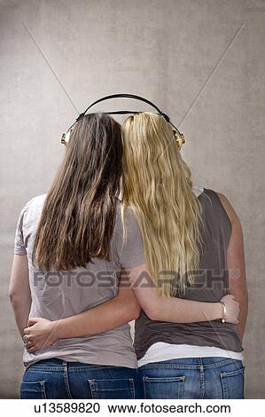 Stock Image - Teen girls share headphones. Fotosearch