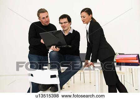 Stock Photo - Three business people look at laptop. Fotosearch