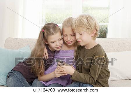 Three children looking at a mobile phone View Large Photo Image Stock Image - Three children looking at a mobile phone. Fotosearch