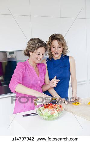 Stock Image - Two woman preparing salad with vinegar. Fotosearch