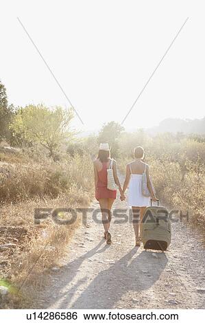 Stock Photograph - Two women pulling suitcases along a lane. Fotosearch