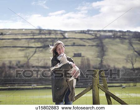 Stock Image - Woman holding lamb in front of fence. Fotosearch