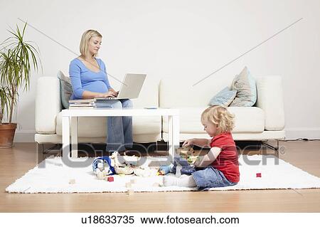 Stock Photography - Woman on a laptop at home with toddler. Fotosearch