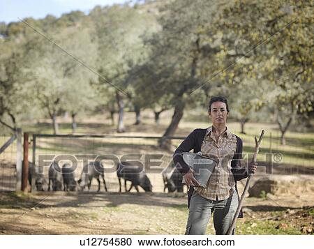 Stock Image - Woman on farm holding bucket and stick. Fotosearch