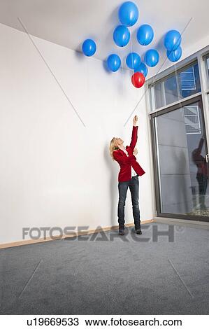 Stock Image - Woman picking red balloon from ceiling. Fotosearch