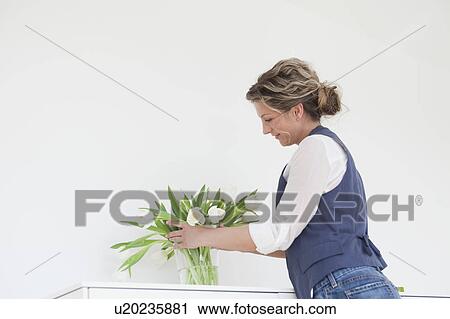 Stock Image - Woman putting tulips into a vase. Fotosearch
