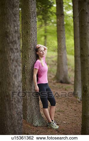 Stock Image - Woman running, standing against tree. Fotosearch